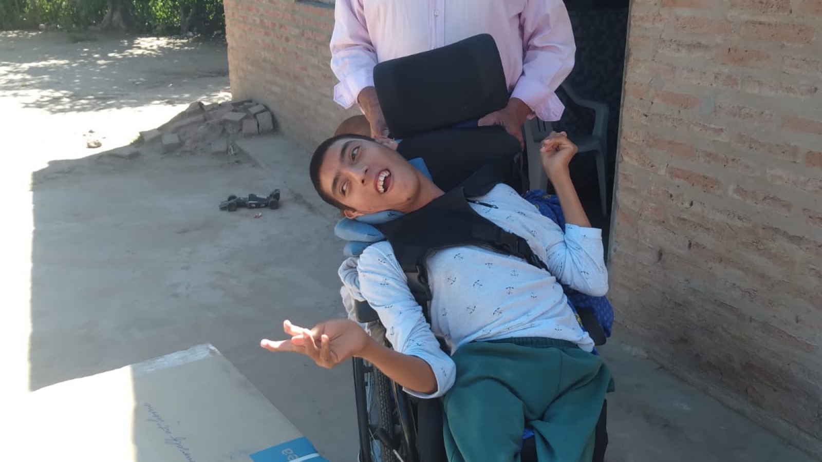 Persona parada con su hijo en silla de ruedas sonriendo frente a cámara